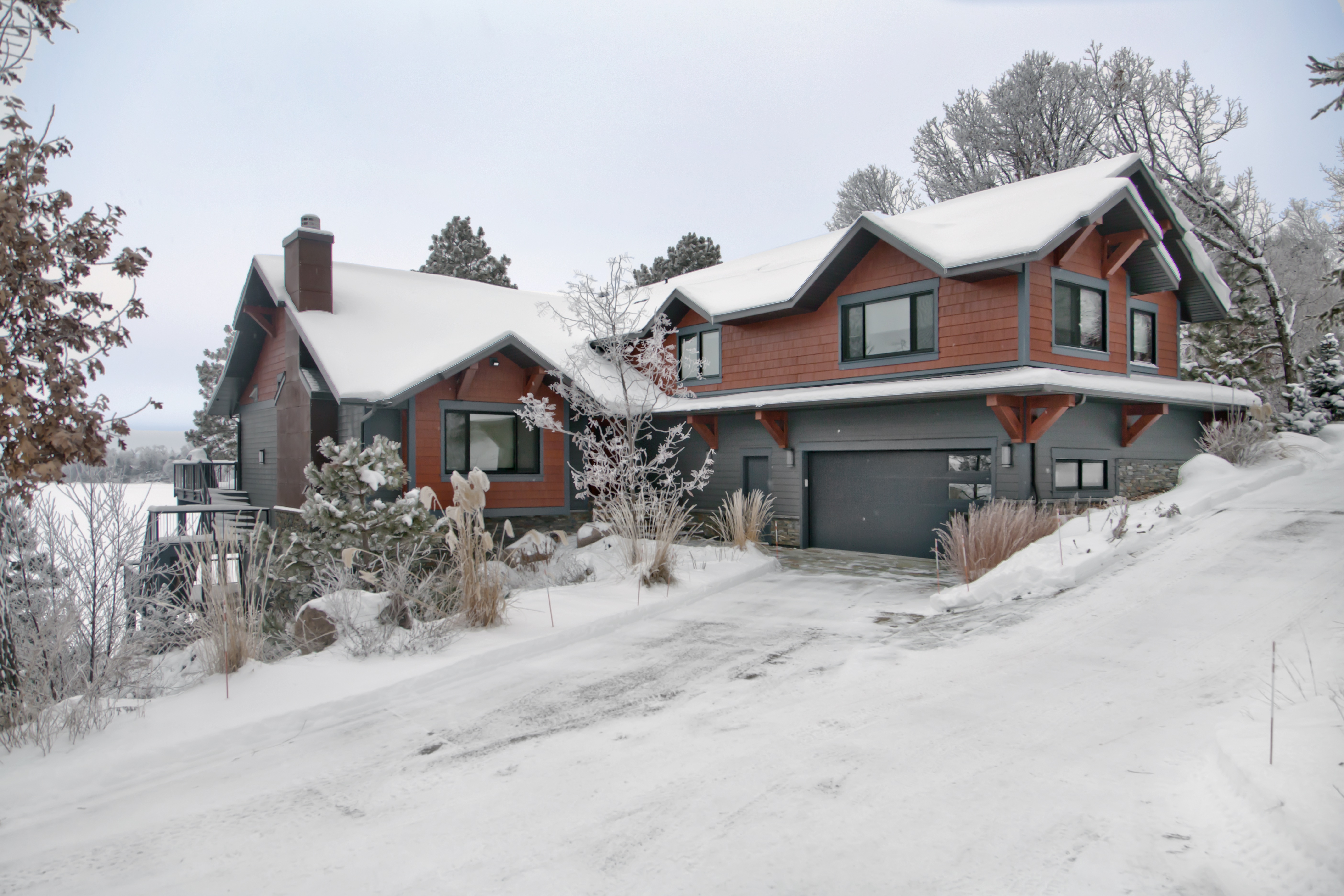 Custom home with reddish-brown fiber cement siding and gray accents overlooking a snow-covered lake.
