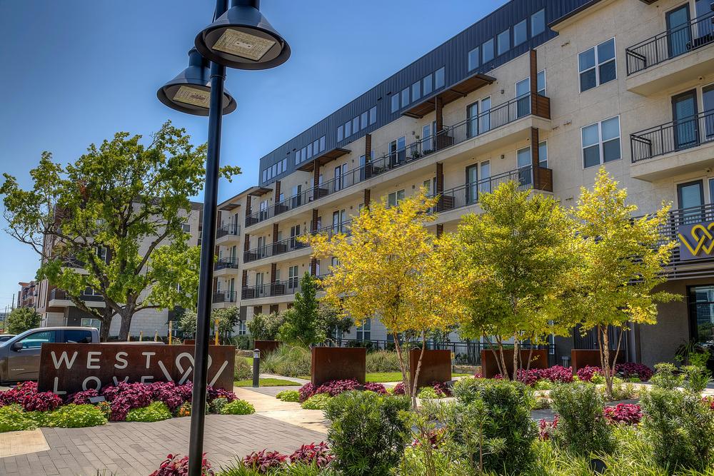 10 West Love apartments in Dallas with Nichiha&rsquo;s fiber cement cladding and many trees, flowers and bushes in front of the building.