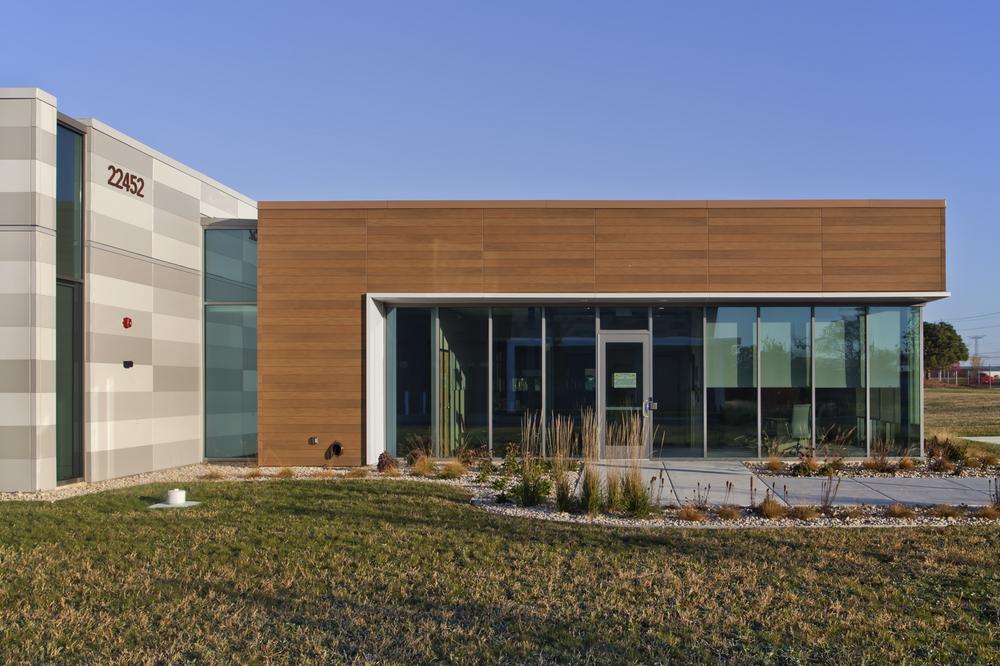 The side entrance of an office building, with large windows surrounding the door next to VintageWood and Illumination siding in shades of tan.