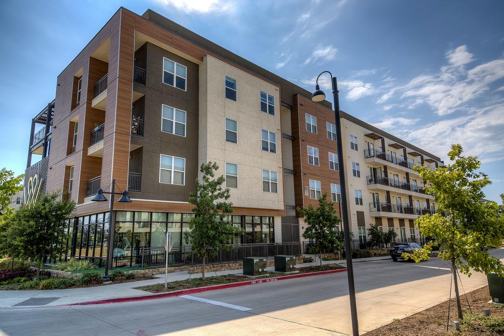 A commercial space (shops and apartment building) featuring an exterior building design with fiber cement siding that&rsquo;s highlighted by wood and earth tones.