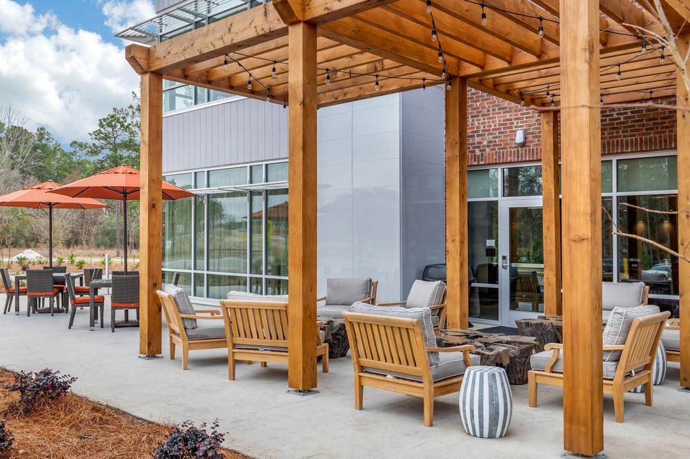 A ground-floor look at the back patio of a hotel, featuring wood pergolas, orange umbrellas and brown wooden patio furniture. 