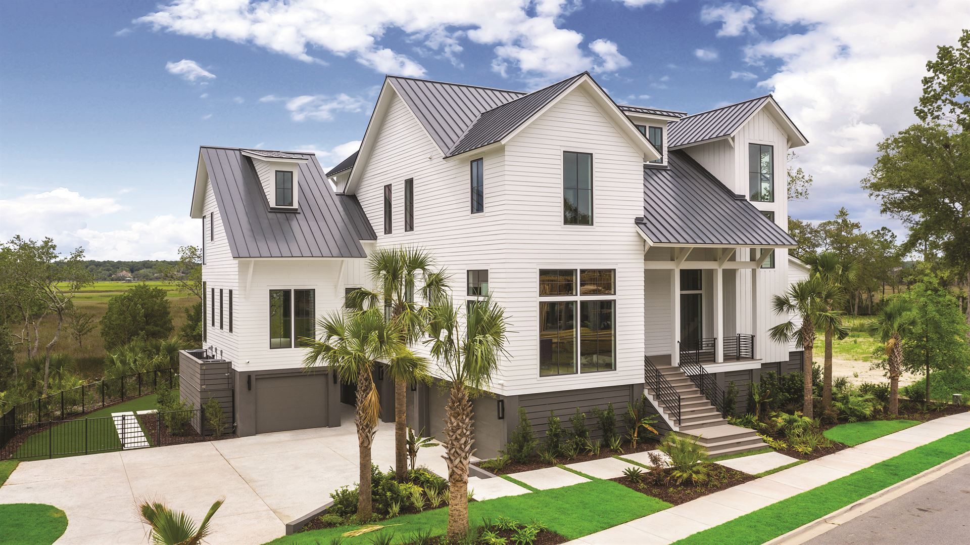 A side look at a home with NichiPanel primed siding painted white and a black roof, along with black framed windows, surrounded by palm trees and green grass.