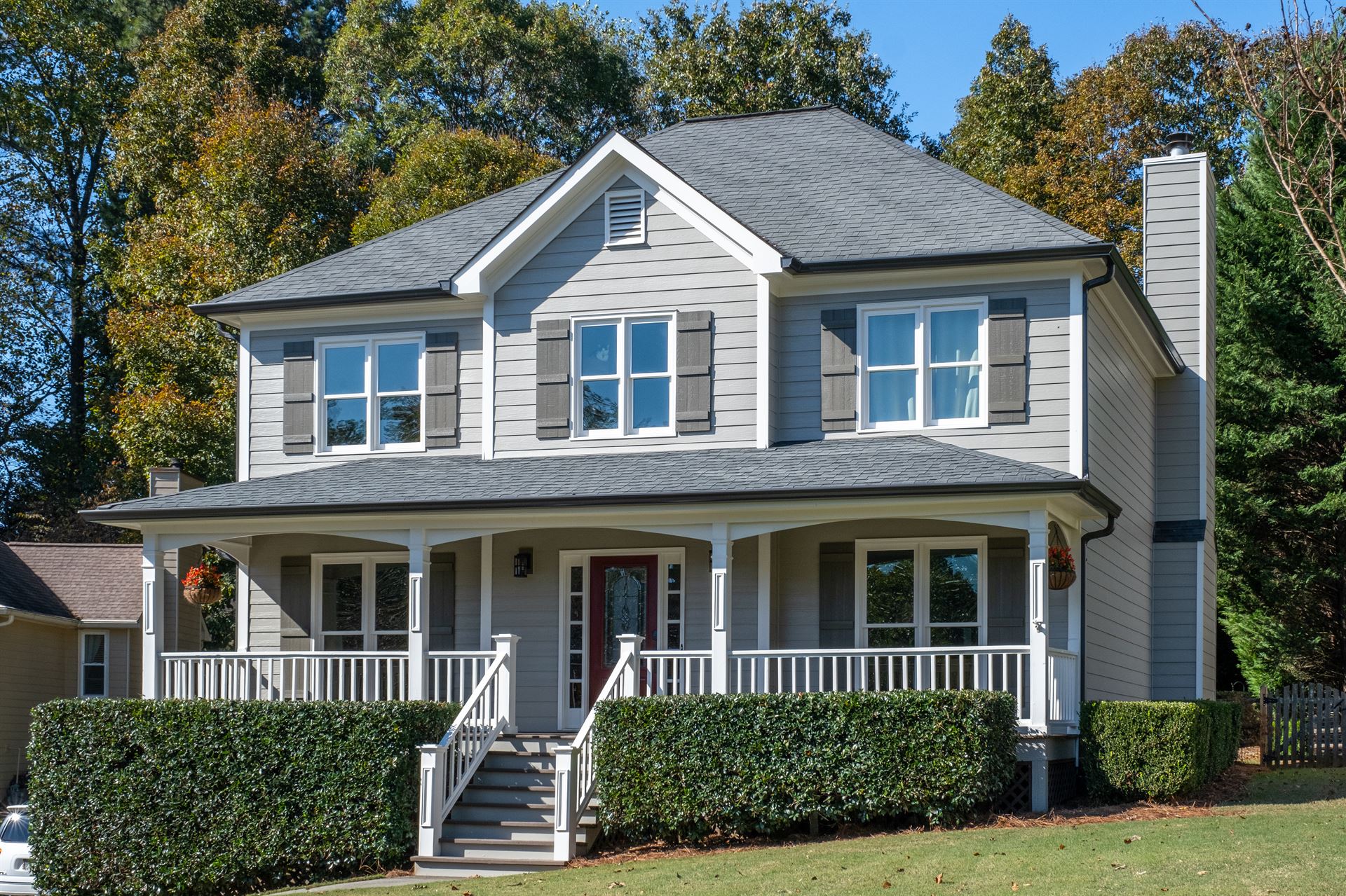 A traditionally modern home with light grey fiber cement siding, white-framed windows, black shutters and a large white front porch.