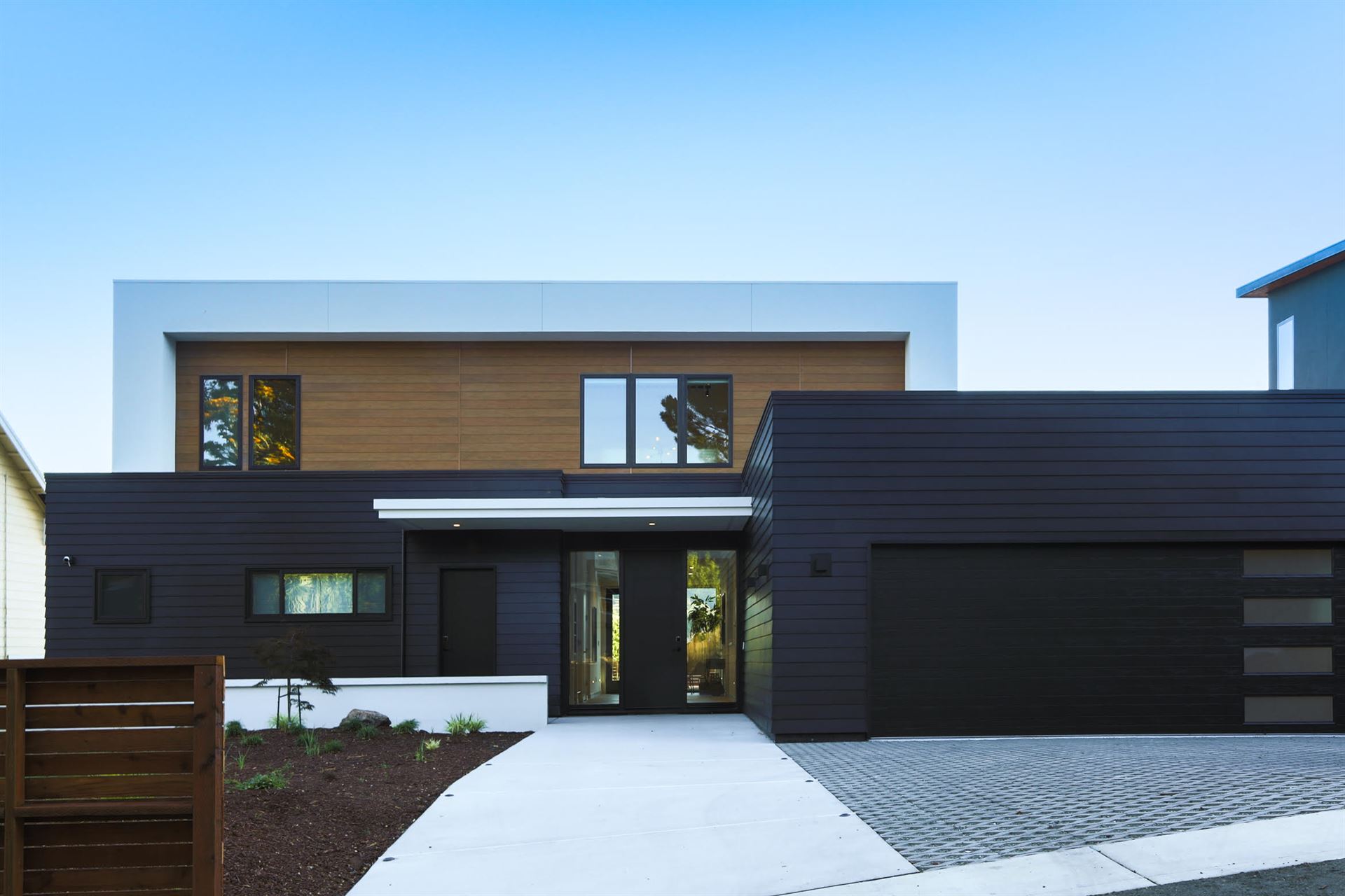A home with ultra-modern architecture, featuring black siding on the first floor to complement the black garage and front doors and light wood-textured siding on the second floor.
