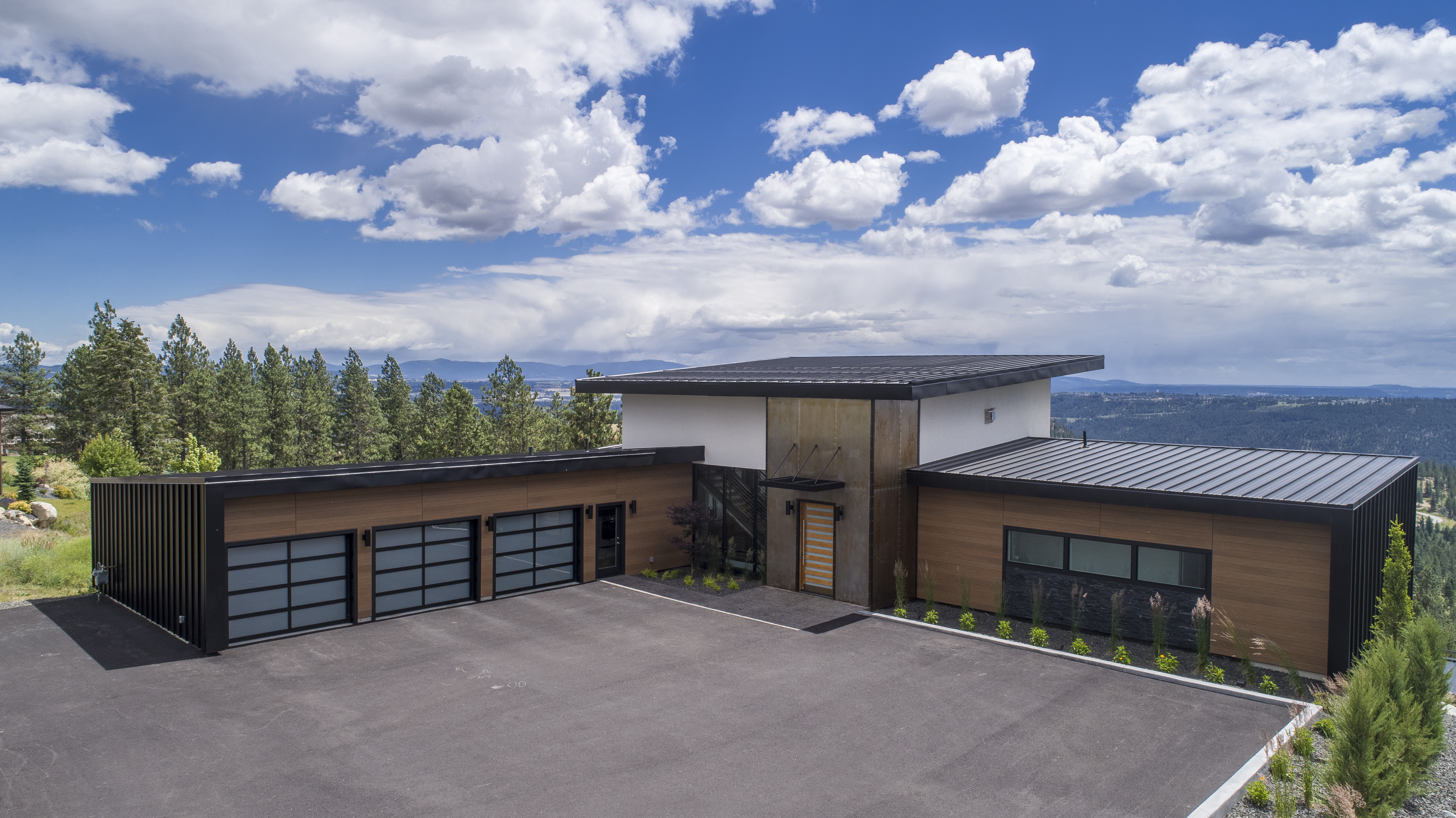 A wide, top-down view of a residence with a three-car garage, large driveway and overlooks mountain scenery.