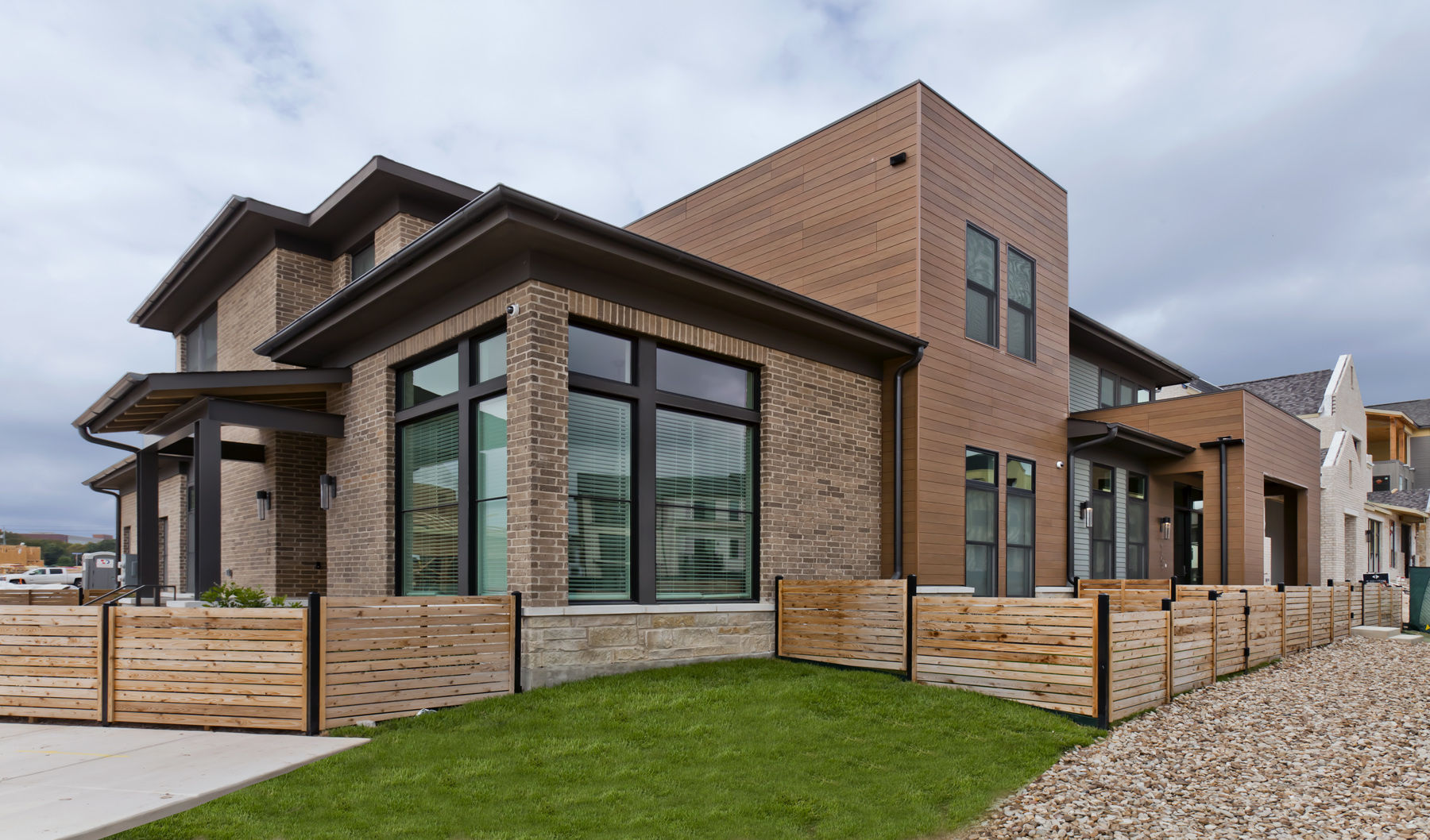 Residence with brown and brick siding, a wooden fence and large windows.