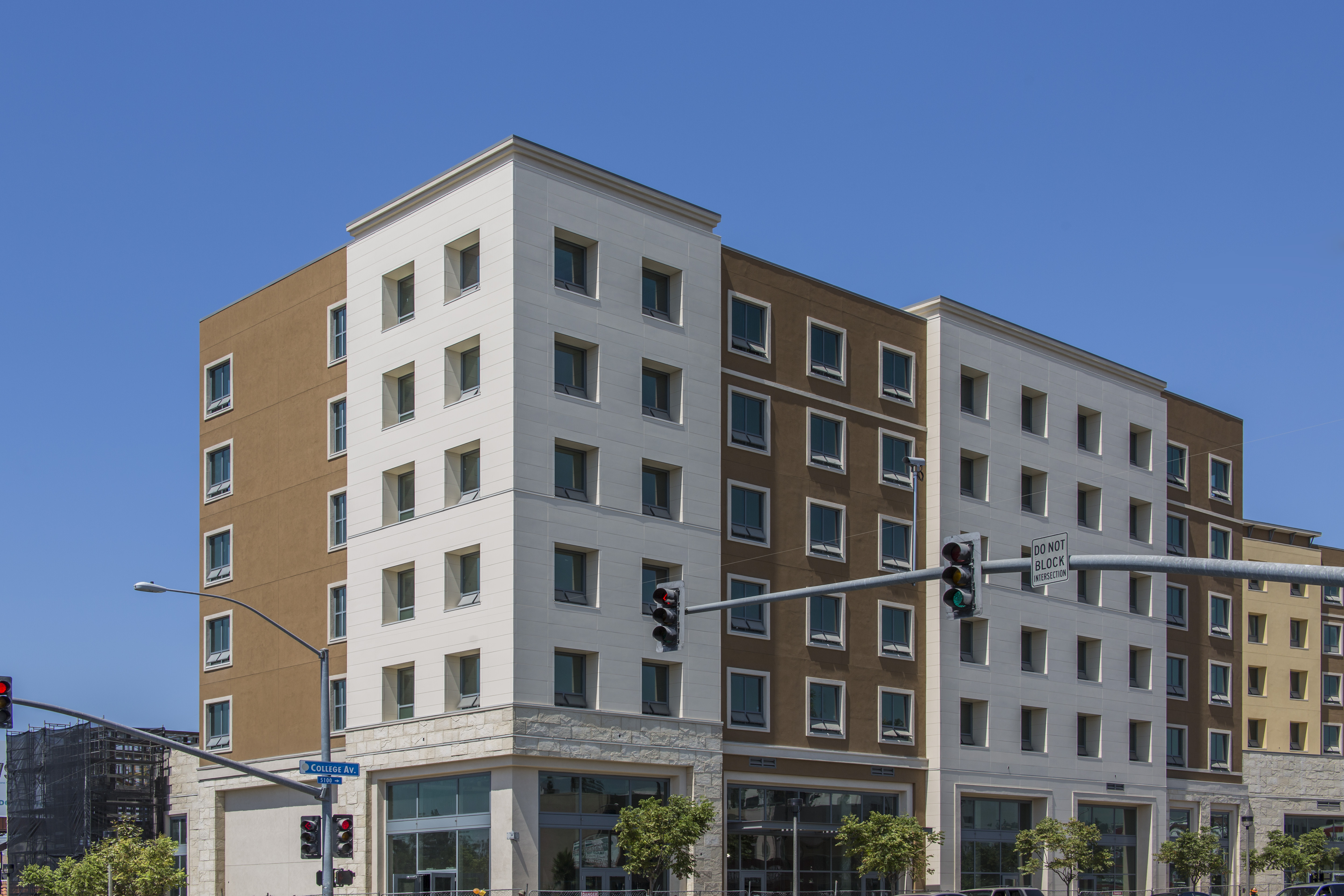 Street view of student housing highlighting new siding with stoplight and trees by the building.
