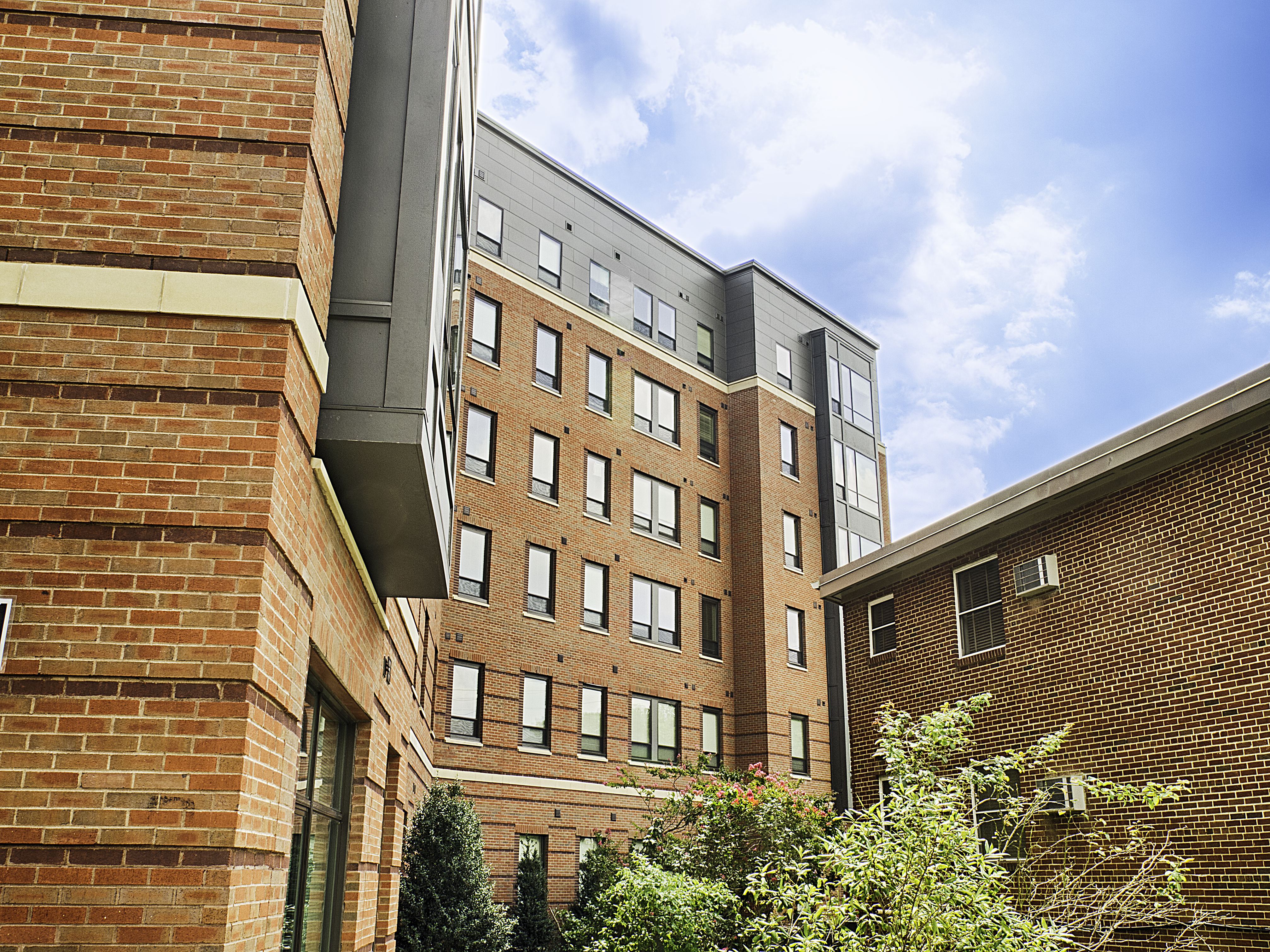Tall, brick student housing with trees and plants by the windows.