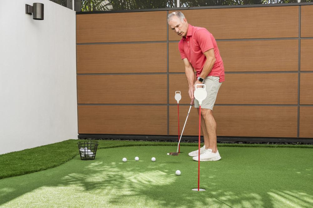 A man on a backyard golf green course hitting a golf ball in front of a wall utilizing Nichiha&rsquo;s RiftSawn fiber cement cladding.