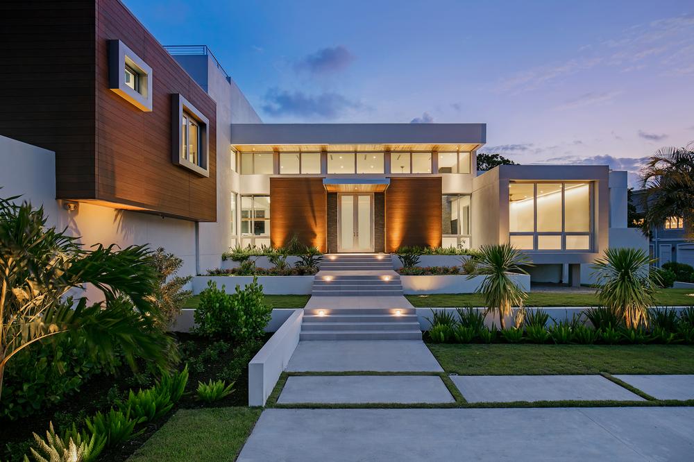 A modern home with a white exterior and wood exterior accents using fiber cement panels. A stairway leads up to the front door and landscaping flanks the pathway to the door.