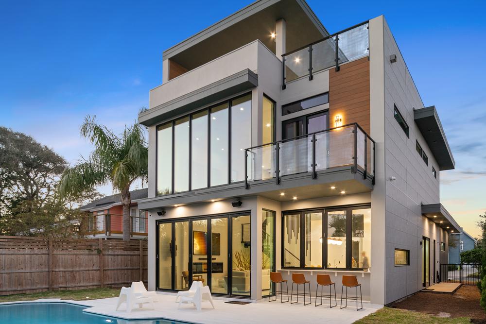 Three-story home full of tall windows looks to backyard pool with palm trees.
