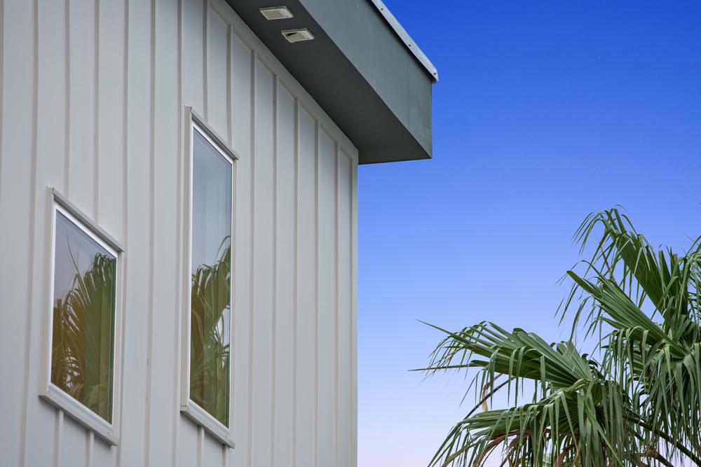Square-roofed home with dark and light gray siding with palm trees in the yard.