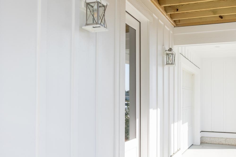  Home patio with white board and batten siding and metallic light fixtures.