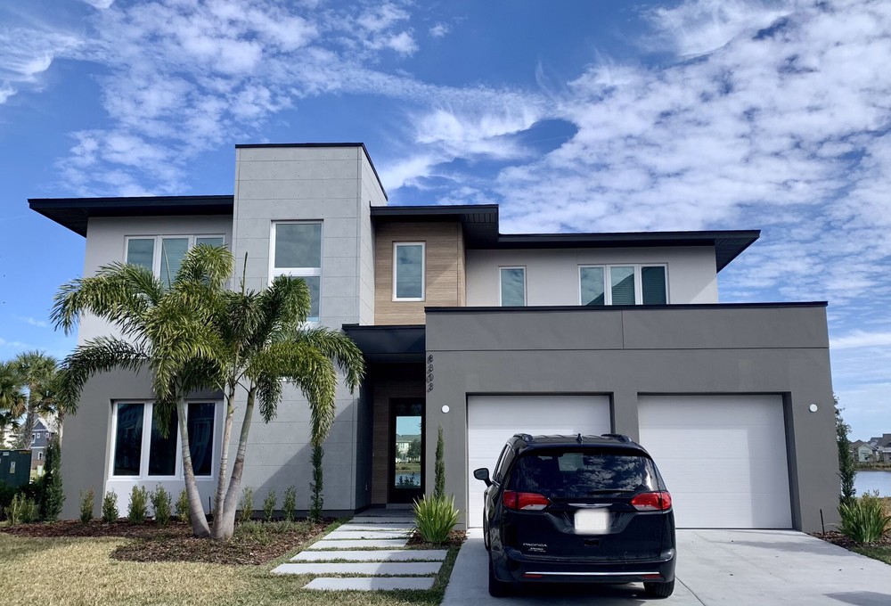 Square-roofed home with dark and light gray siding with palm trees in the yard.