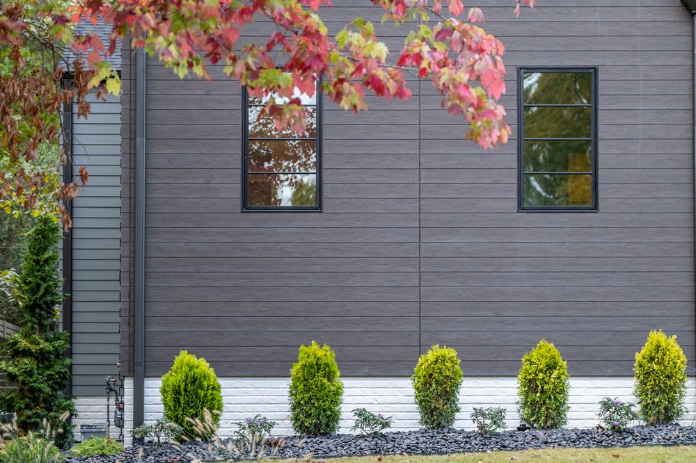 Home exterior with grey and brown siding lined by green shrubbery.