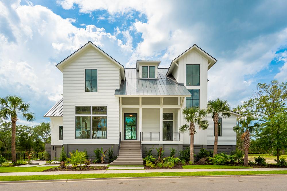 This large white house has fiber cement siding. There are brown steps leading to the front door and a small patio area. There are rectangular windows on the front of the home, and there are palm trees in front of the home.