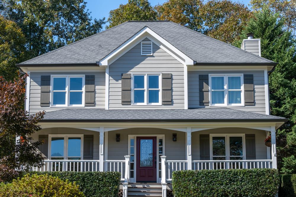 A two-story home with light gray siding, dark gray shutters and white trim. The front door is a dark red.