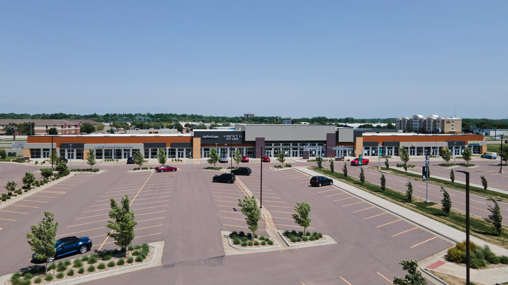A faraway shot of a strip mall at South Lorraine Place utilizing Nichiha&rsquo;s fiber cement cladding. A large parking lot with a few cars in front of the strip mall.