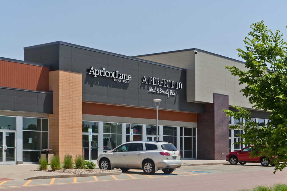 A close-up shot of the strip mall at South Lorraine Place. There are signs for Apricot Lane and A Perfect 10 Nail & Beauty Bar with the exterior utilizing Nichiha&rsquo;s fiber cement cladding in different textures.