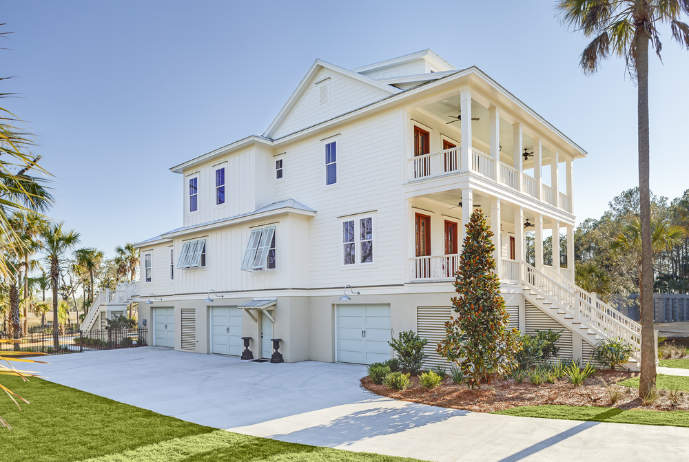 This white, three-story house has two large front porches. There is a paved driveway leading to the three garages.