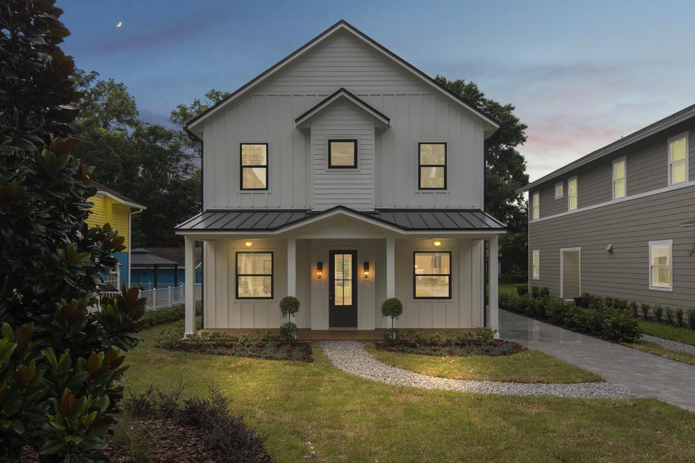 This white, two-story house has a large front porch. There is a gravel walkway leading to the front door. There are flower beds on both sides of the walkway.