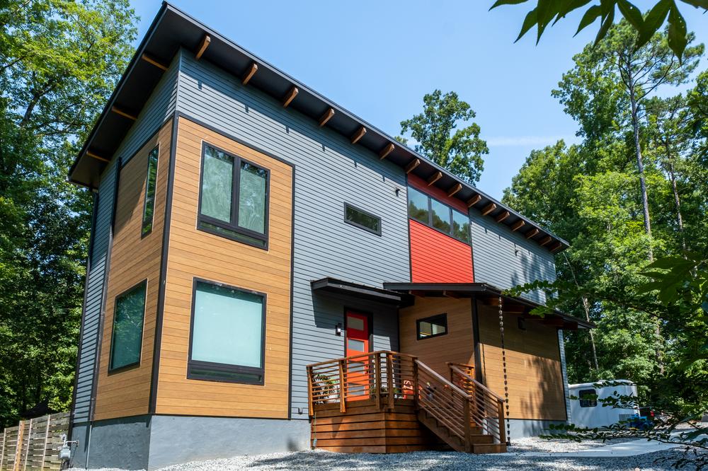 A gray house has Nichiboard and accents with VintageWood in Cedar. This is a two-story house with a porch area.