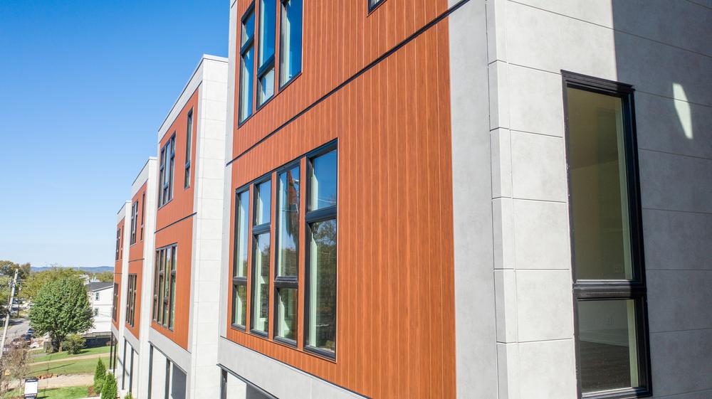 These apartments look out onto a street view. They have vertical wood-like siding.