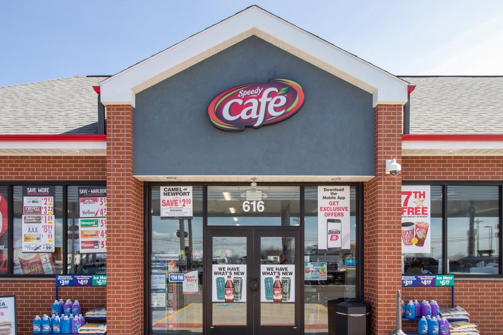 Speedy Cafe convenience storefront with red brick, sale signs and washer fluid bottles on racks.