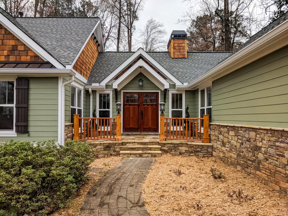This green, rustic home features fiber cement siding. The green siding contrasts with the warm, rustic wood shake siding on the gables and the cool gray roof.