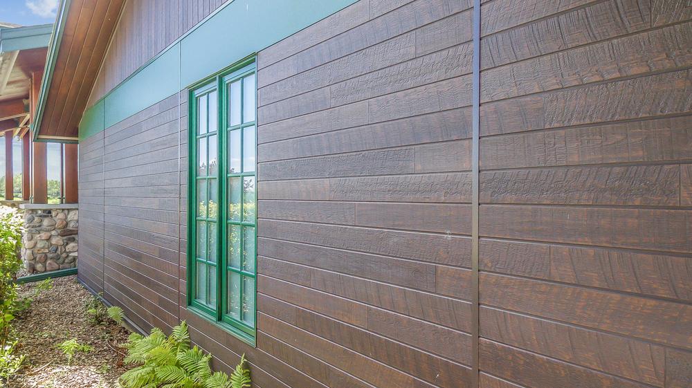 Exterior of home with darkly colored wood look fiber cement paneling and green windows.