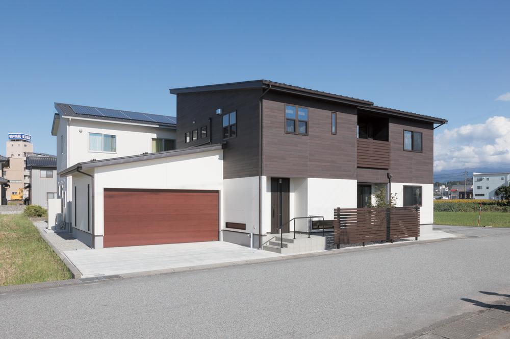 A two-story home with a white garage and red garage door. The second floor is sloped with dark brown siding.