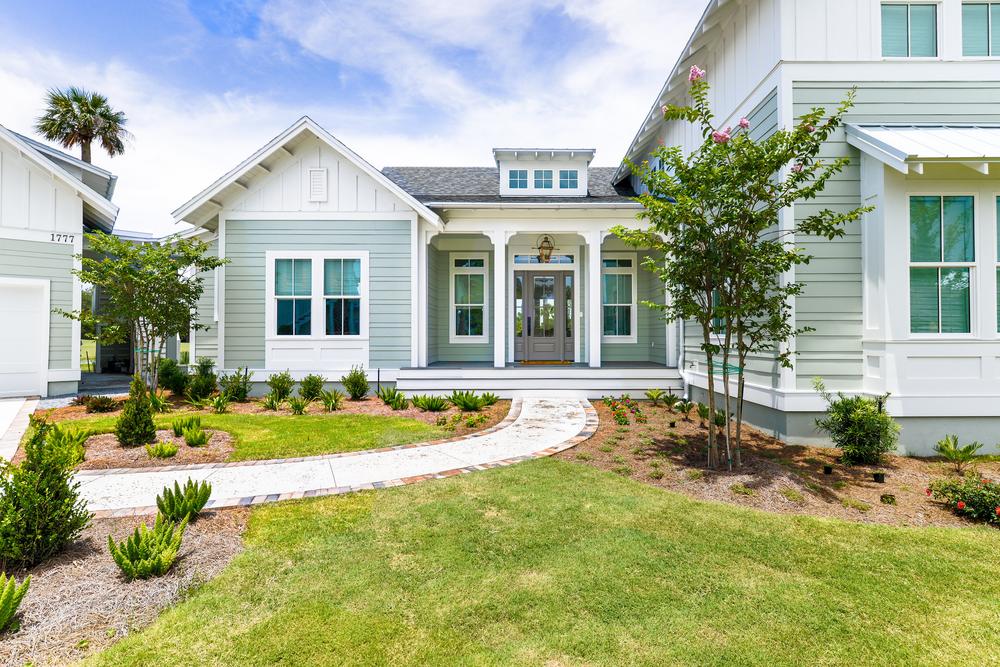 A home with light green and white siding has a front porch with a brown door and hanging light fixture.