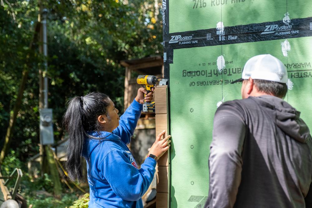 An installer applies Nichiha Vintagewood in Cedar to the corner of a building. Another team member stands next to them.