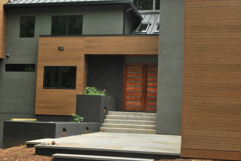 Modern home design with metal roofing, sage green stucco and wood look fiber cement siding.