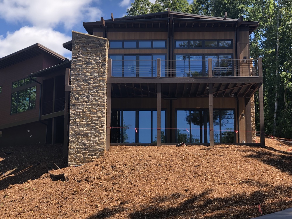 A brown wood sided home in the mountains with a stone pillar and mulch in the yard.