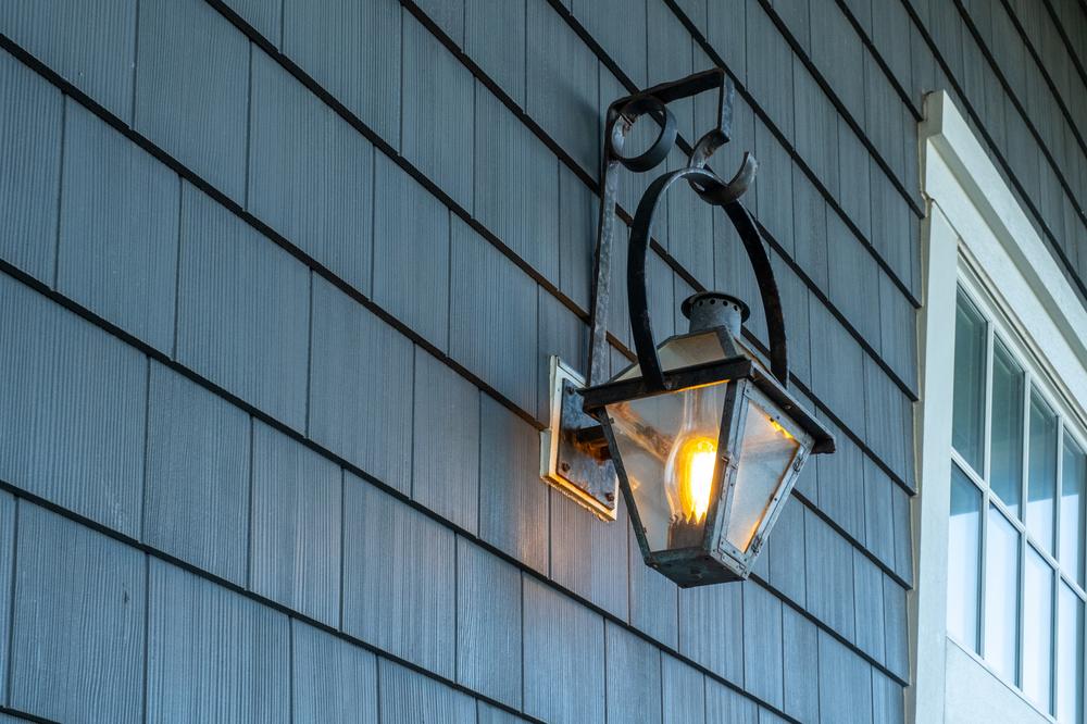 A blue shake-sided exterior wall with a black light fixture and white windows.