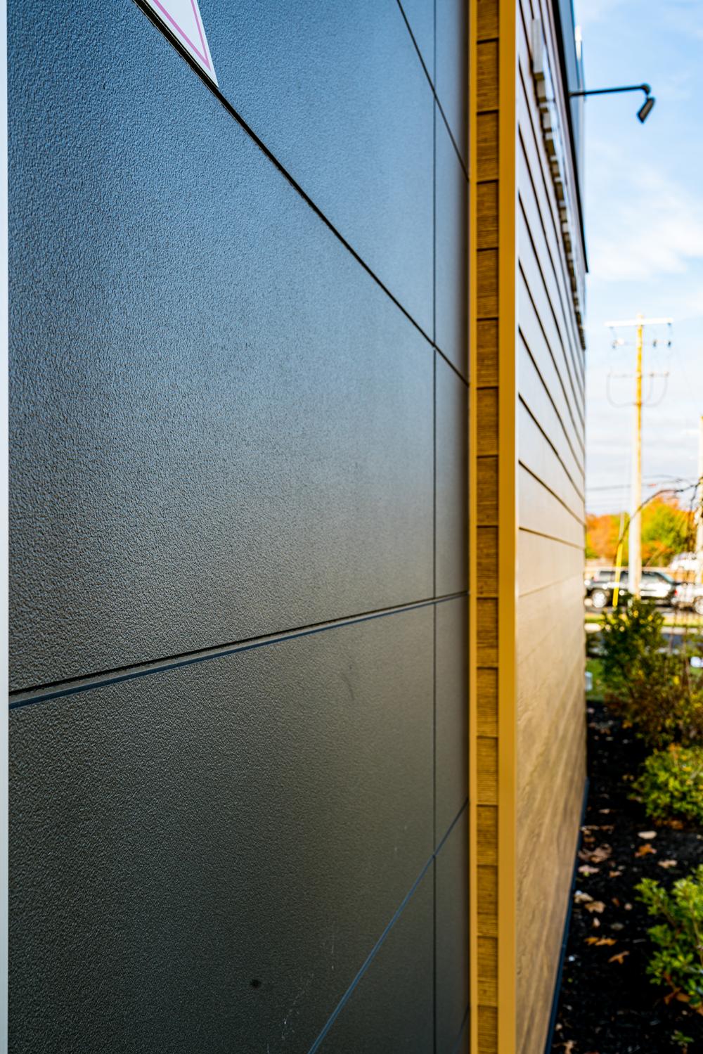 The side of a commercial building with black fiber cement siding under a layer resembling wood.