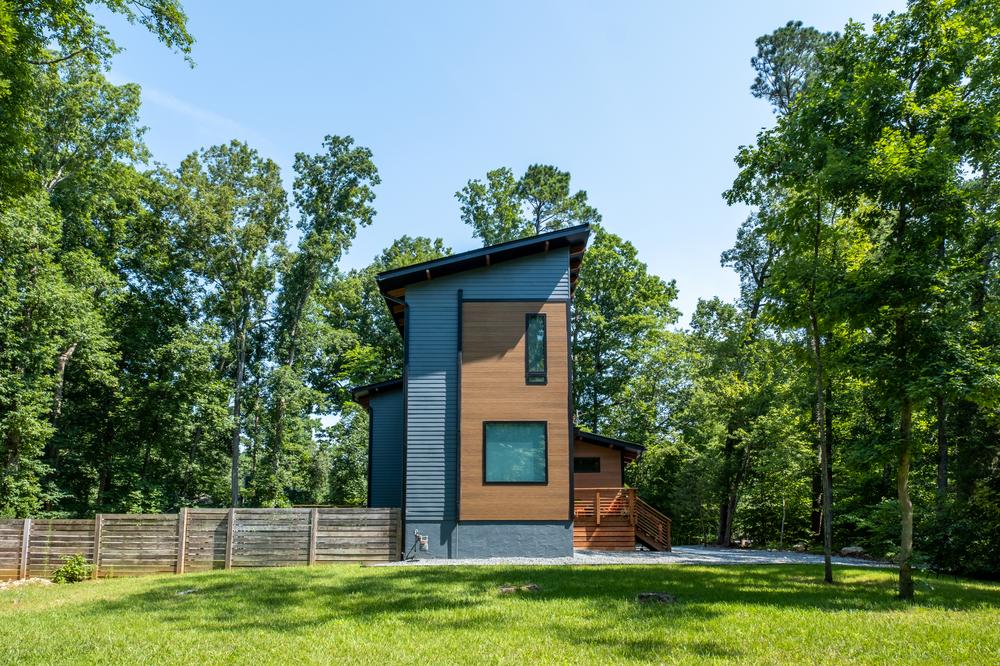 A side view of a two-story home with blue and wood-like siding. There are trees surrounding the property.