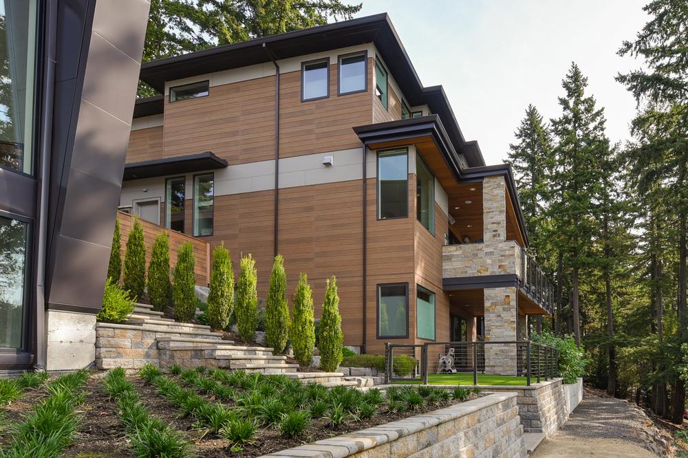 This three-story home has a wood-like exterior. There are trees surrounding the home.