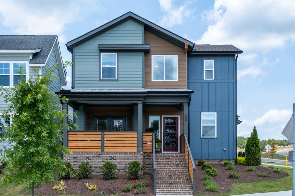 This two-story home has blue and wood-like siding. Brick steps lead up to the home&rsquo;s front door and front porch.