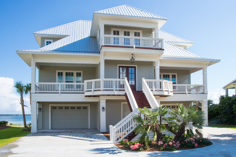 This neutral-colored, three-story house has two attached garages, three balconies and a paved driveway. It is located on a waterfront property in Florida.