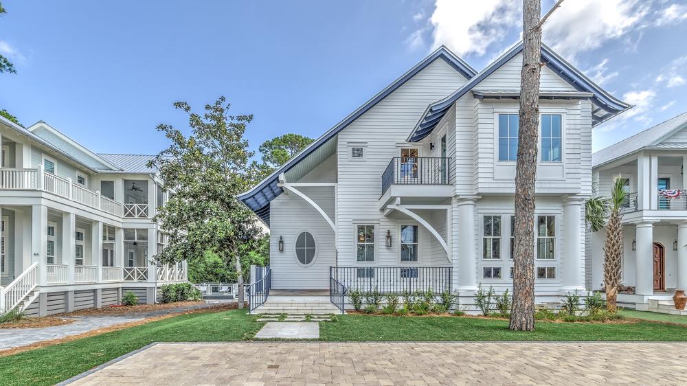 This two-story white house has black railing systems, large windows, green grass and a concrete pad for parking.