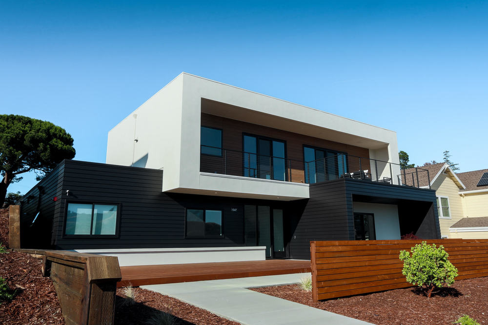 This modern home has white, black and wood-like siding. There is a wooden fence in front of the home.