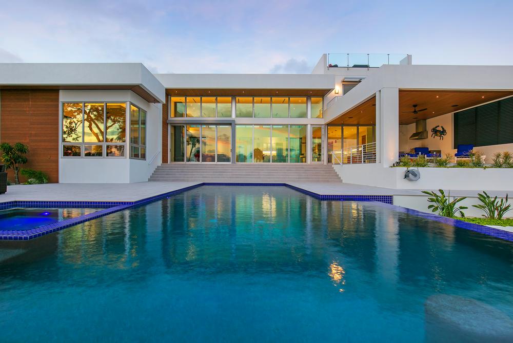 This modern home has a large pool. There is an outdoor seating area, and the home has wood siding accents.