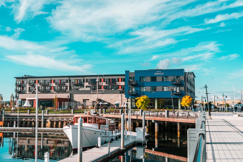A hotel located right next to the water with a boat and dock near the hotel and some trees above the dock.