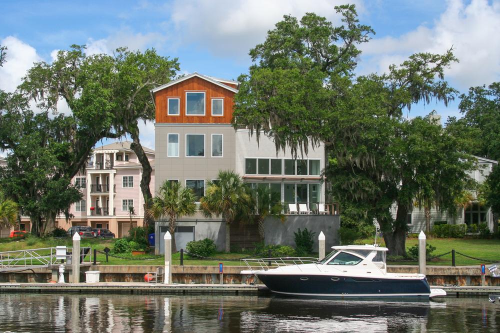 A home sitting on the water with Spanish moss and palm trees by the home, and a large boat docked close to the house.