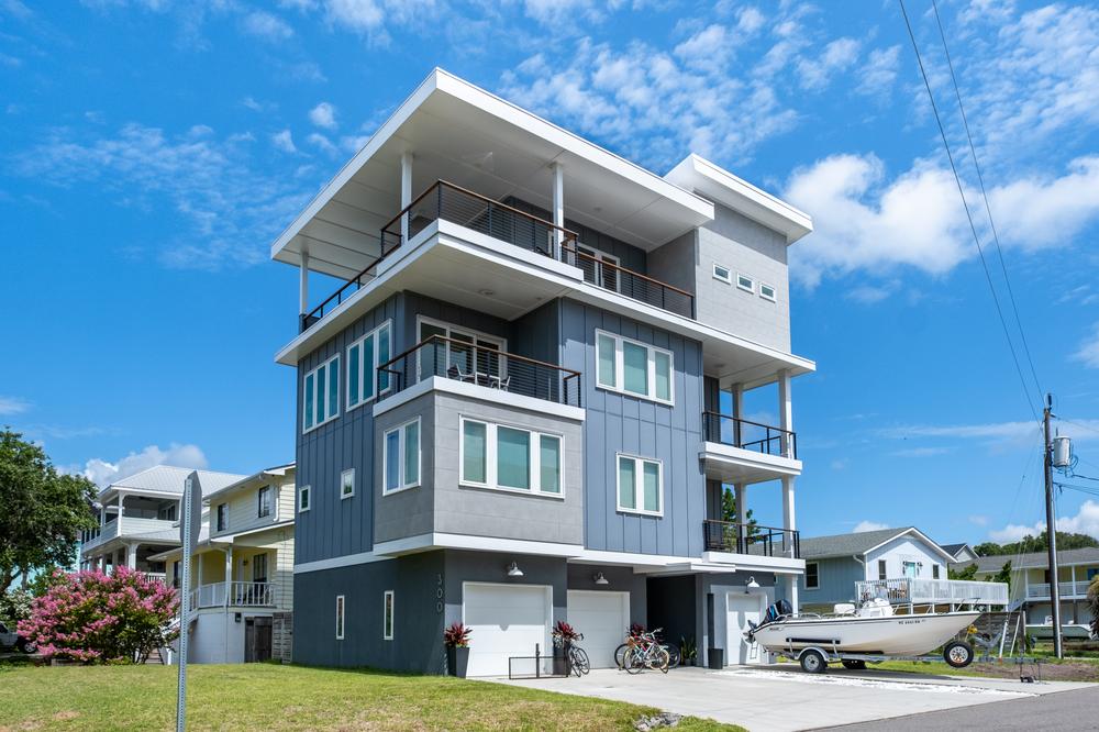 This four-story home with grey and blue siding has a boat in the driveway.