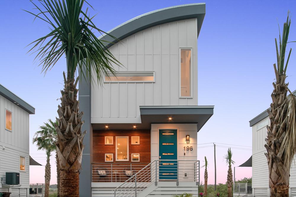 Residential home with a curved roof and blue door surrounded by palm trees.