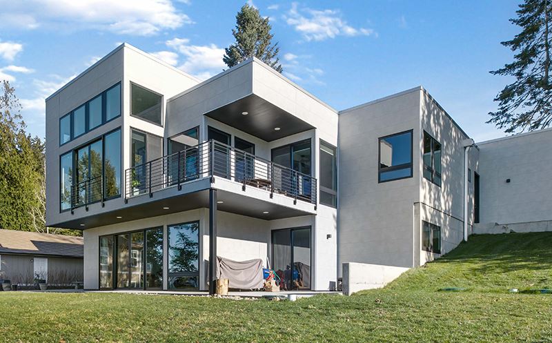 Back view of a boxy modern home with gray, concrete-texture fiber cement siding and black railing