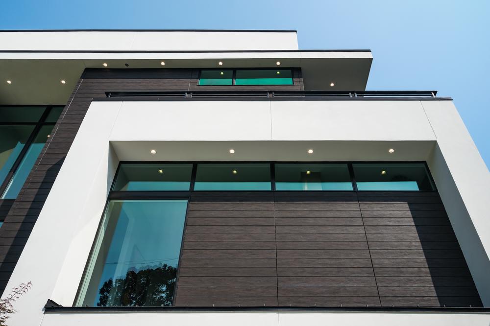 Outside shot of a home with a contemporary design, featuring white concrete-style and dark brown wood-textured fiber cement with trees in the backyard and stone steps leading to the door.